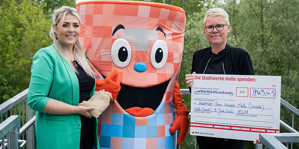 Mitarbeiterin der EVH und Maskottchen Thermo-Toni übergeben Spendenscheck an eine Mitarbeiterin des Hospizes.
