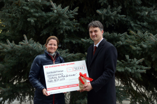 Vor einem Weihnachtsbaum übergibt Matthias Lux ein kleines Säckchen mit den Spenden an Johanna Ruoff.