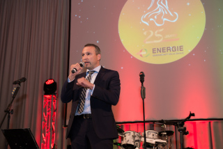 EVH-Geschäftsführer Olaf Schneider steht auf einer Bühne spricht zu den Gästen. In seiner rechten hand hat er ein Mikrofon. Der Hintergrund leuchtet in einem sanften rot-gold.