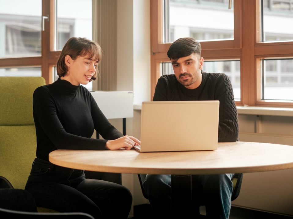 Zwei Mitarbeiter sitzen an einem Tisch und schauen auf einen Laptop